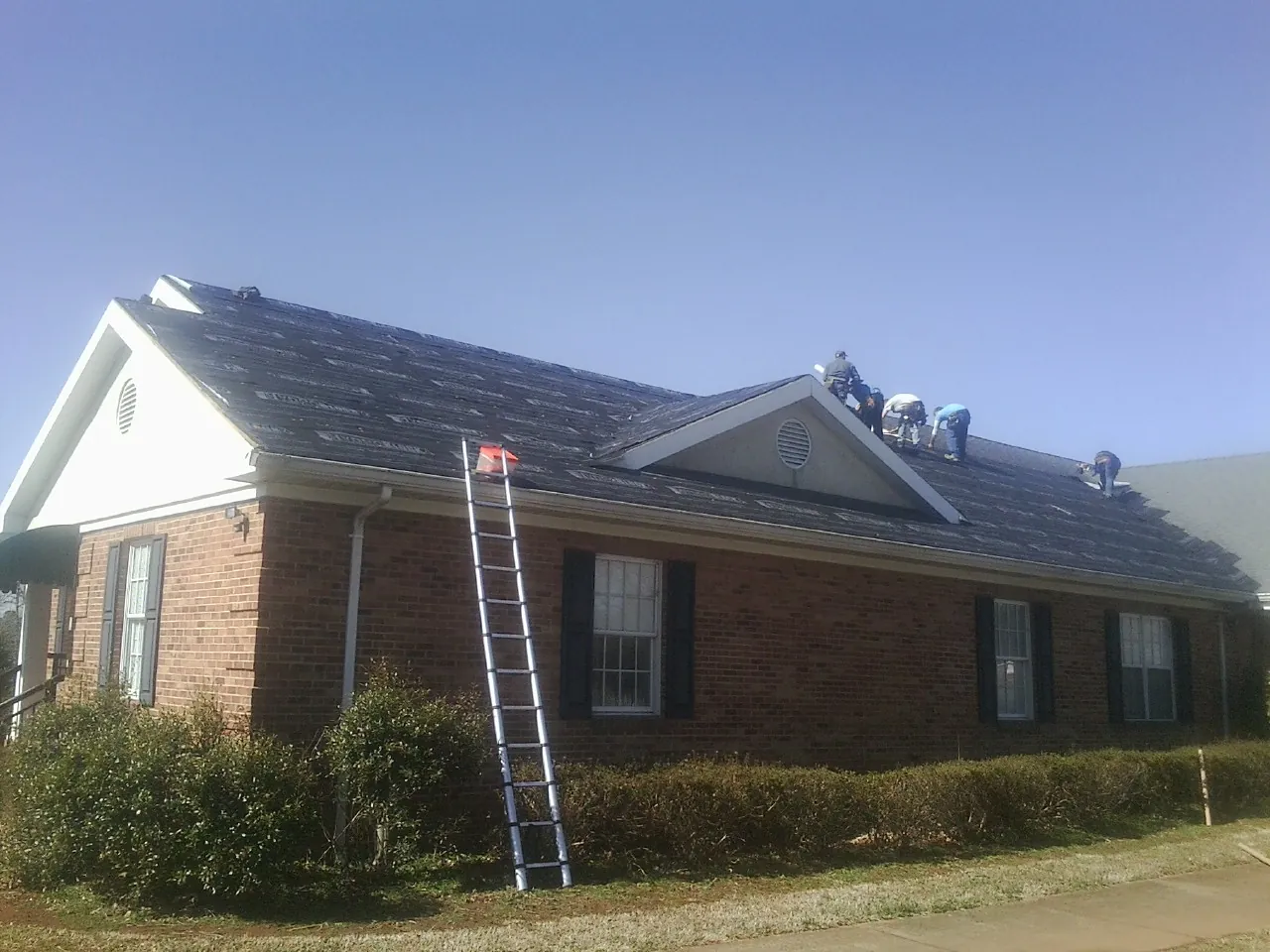 Crew tearing shingles off a brick ranch roof with a ladder set in Cayuga